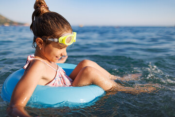 Cheerful girl sits in an inflatable circle and splashes with water in the sea