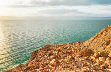 Fototapeta na wymiar Dead sea shore at Jordan side, dry sand and rocks beach, sun shines on beautiful azure water surface