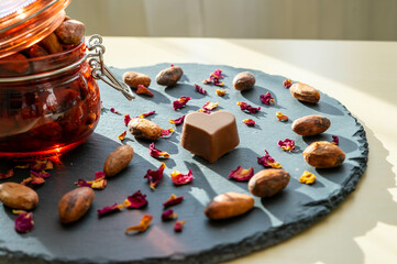 Chocolate heart and cocoa beans , with a jar filled with cocoa beans and rose petals on a slate plate