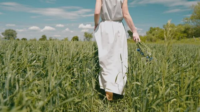 a beautiful woman in a simple linen dress in a field with a bouquet of wildflowers in her hands, the concept of summer walks, folklore simple style