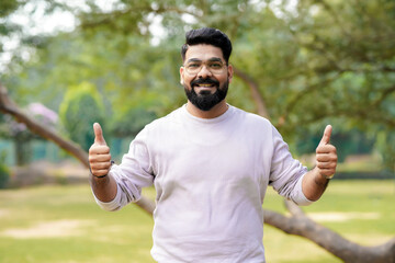 Young and confident indian man showing thumps up at park.