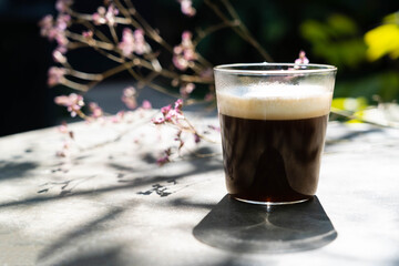 A cup of americano macchiato coffee  with  blur pink flower in the background in the morning