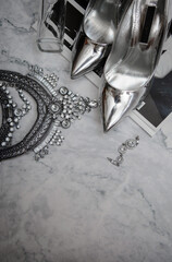 Woman party accessories set. Clamor shoes heels. Silver shoes on marble background.Flat lay, top view