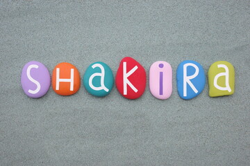 Shakira, female given name composed with multi colored stone letters over green sand