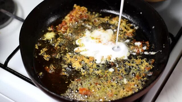 Deglazing the frying pan with coconut milk. Pouring milk on ginger and garlic pieces. Cooking a sauce or curry