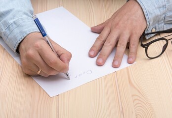 write a letter. In the hands of a man is a ballpoint pen and he writes a letter. Wedding ring on...