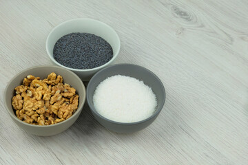 Vegetarian product. Ingredients for adding to baking. Poppy seeds, coconut shavings and walnut in bowls on a woody background. Copy space.