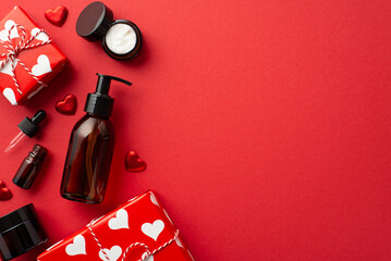 Natural cosmetics concept. Top view photo of gift boxes amber pump bottle without label dropper bottle cream jars and hearts on isolated red background with copyspace