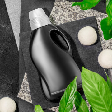 Natural Laundry Detergent Mockup For Washing Black Clothes. Washing Detergent Concept With Bottle Of Washing Gel Or Fabric Softener On Textile Napkins On Black Background With Plants. Laundry Day