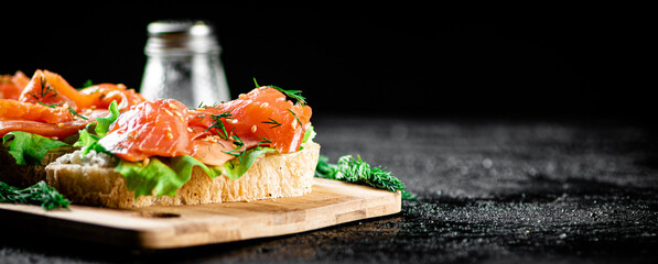 Sandwich with pieces of salmon on a cutting board. 