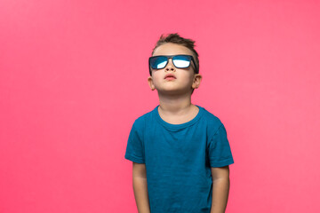 Little boy in sunglasses posing in studio on pink background. Copy space