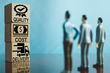 A group of business professionals focus on wooden cubes displaying the QCD (Quality, Cost,...
