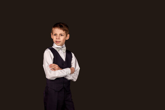 Serious schoolboy in school uniform on black isolated background. Fashionable little boy wear suit with bow tie, student crossed hands looking away in studio. Education concept. Copy text space for ad