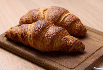 Baked crispy croissant on a wooden board, breakfast.