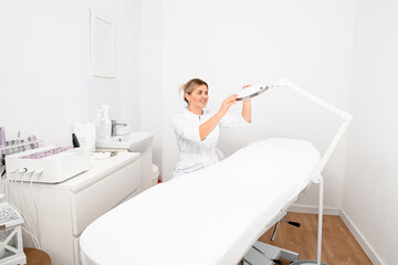 great view on attractive woman cosmetologist accurate fixing lamp on examination couch in beauty clinic.