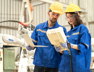 Industrial engineer using remote control board to check robotic welder operation in modern automation factory. Male and female technician monitoring robot controller system for automated steel welding