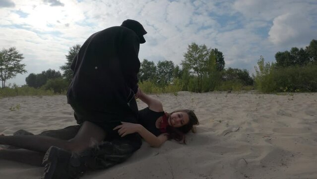 Cinematic shot  maniac chasing victim in a wasteland outside the city. Tall man in black clothes with rope in hands fighting with girl in red jacket, sneakers and long hair. True crime concept 