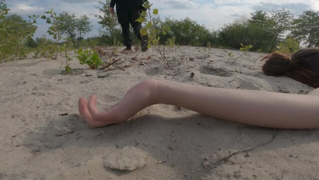 Maniac who committed murder leaving scene of crime. Tall man in black clothes with a rope in his hand steps over the corpse of a young girl lying on the sand in a wasteland outside the city.