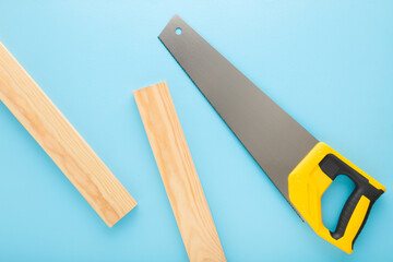 Hand saw and wooden planks on light blue table background. Pastel color. Closeup. Top down view.