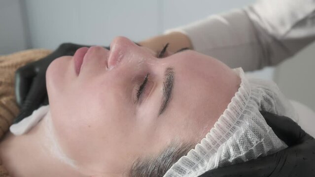 Profile portrait of relaxed woman's face, cosmetologist removes skincare product