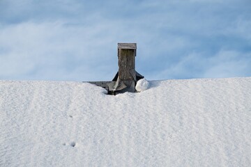 Fototapeta premium The roof is covered with snow, with a wooden chimney and a blue sky with clouds.
