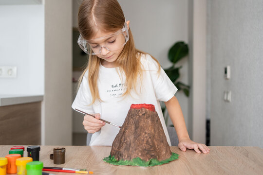 child make volcano for science experiments. Kid girl make volcano model, painting it.