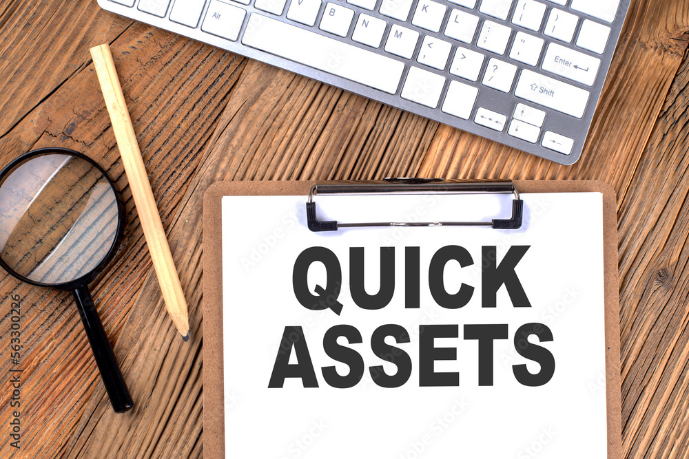 Poster quick assets text on paper clipboard with magnifier and keyboard on wooden background