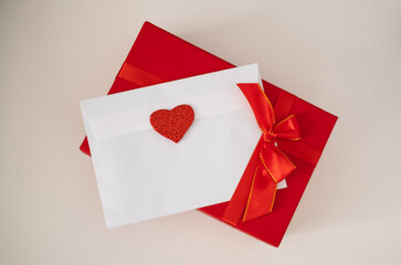 Romantic love letter in white envelope with Valentines heart and gift box with red ribbon on white background. Flat lay, top view. Happy Valentine's Day concept
