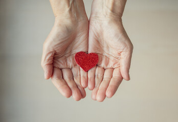 Female hands holding little red heart. Old woman's hands giving care and love. Mother's love...