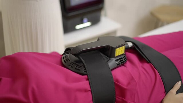 Young woman lying at beauty spa, getting ems treatment or therapy on her abdomen to burn fat and build muscles