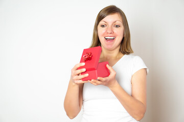 Young brunette girl in white shirt opening a red present box and smile.