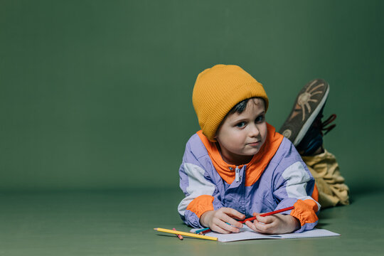 little boy lies on the floor and draws with pencils on green background