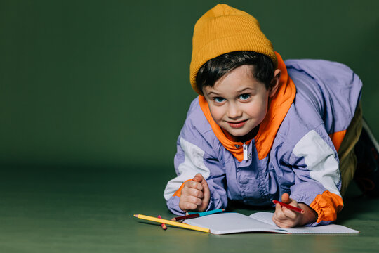 little boy lies on the floor and draws with pencils on green background