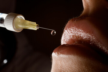 close-up view of syringe needle with drop of the drug near the female lips. Lip augmentation.