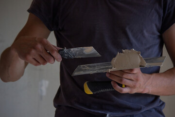 A man holds a spatula with putty in his hands. Selective focus.