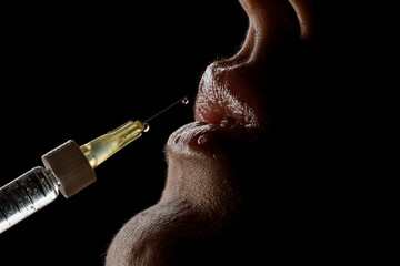 close-up side view of syringe needle with drop of the drug near the female lips. Lip augmentation.