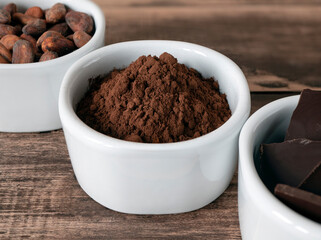 Cocoa powder in the bowl and other chocolate products on the wooden table. Cacao powder, cocoa beans and dark chocolate