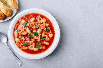 Tomato soup. Minestrone soup. Tomato bean and pasta soup bowl with toasts on gray stone background.