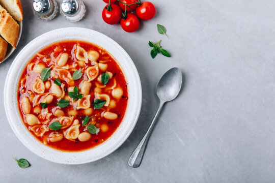 Tomato soup. Minestrone soup. Tomato bean and pasta soup bowl with toasts on gray stone background.