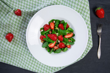 Tasty strawberry salad with nuts and rocked salad on black background, top view. 
