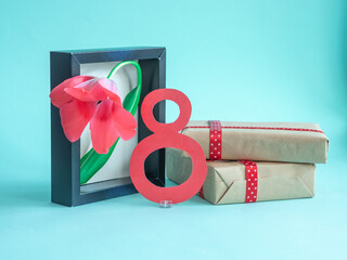 A pink delicate tulip in a cardboard frame stands on a blue background, the number 8, gifts in natural wrapping paper with a red ribbon. Spring creative greeting card for women's Day or Mother's Day