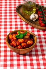 gnocchi with tomatoes and basil in a wooden bowl on a red checkered tablecloth