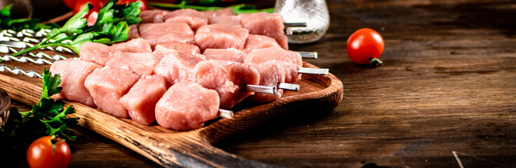 Pork kebab raw on skewers with parsley and tomatoes on a cutting board. 