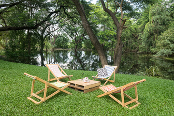 Wooden deckchair and table on green grass by pond