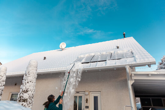 man cleans the panel at rooftop from snow. removing snow off solar panels in winter. Removing snow photovoltaic system - solar cells. snow covers panels - no producing power. energy efficiency 