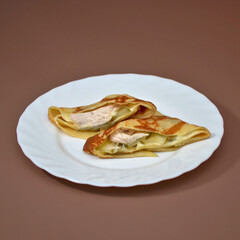 Two ruddy fresh cut pieces of pancake on a white plate, visible filling of chicken, pickled cucumber, cheese, on a brown background