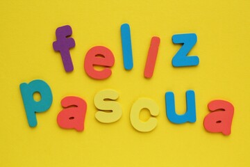 Feliz Pascua, Happy Easter on spanish colored lettering on yellow background. Holiday spring compostion concept. Creative idea for greeting card, poster, banner, invitation. Top view, flat lay