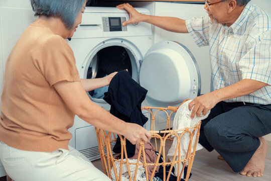Senior couple working together to complete their household chores at the washing machine in a happy and contented manner. Husband and wife doing the usual tasks in the house. - Powered by Adobe