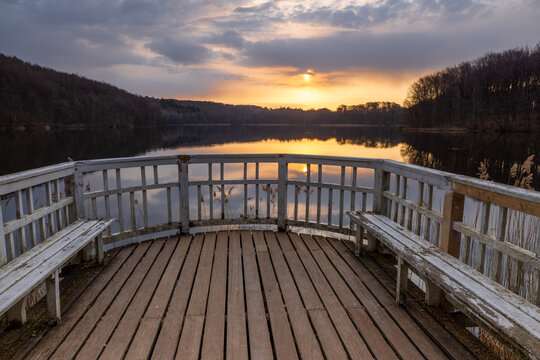 Cloudy sunrise at peaceful and romantic lake Ukleisee with reed and old pier in foreground and forest in background, Eutin, Schleswig-Holstein, Northern Germany