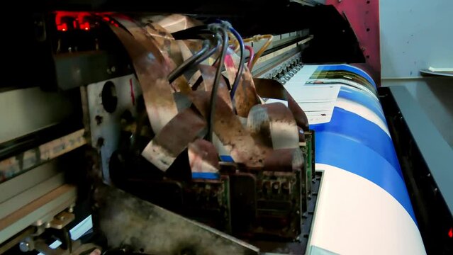 The printhead of a large-format inkjet printer moves along the banner material, an advertising layout is applied with ink. Production of advertising products.